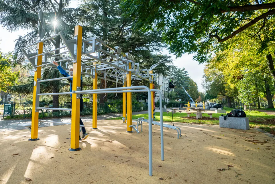 Plan en pied d'un homme utilisant une station de Street Workout Herkules Fitness au Square Tolstoï à Paris