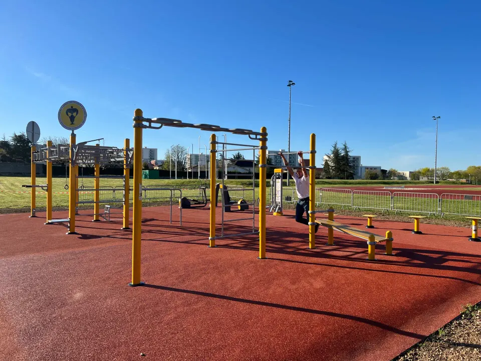 Agrès de fitness extérieur à recharge USB et stations de street workout avec un homme se balançant sur une barre de traction Herkules Fitness sur EPDM à Grand Angoulême
