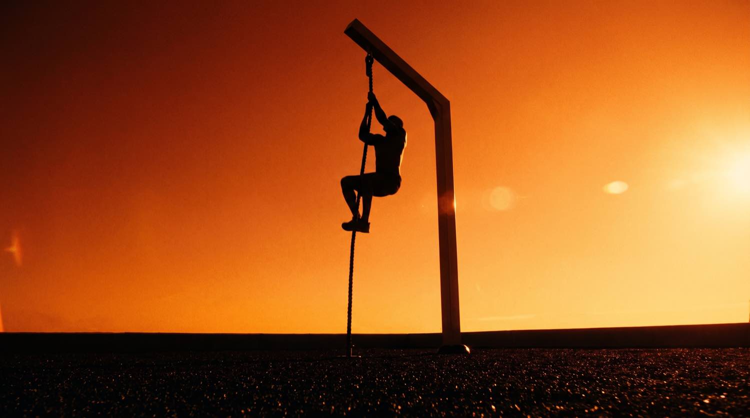 Silhouette d'un pratiquant grimpant à la corde sur un parcours ninja Herkules au coucher du soleil